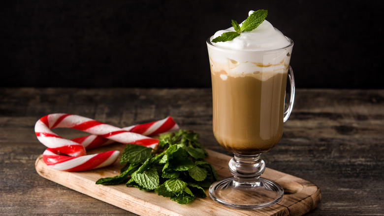 Peppermint mocha with whipped cream next to mint leaves and candy canes on wooden board
