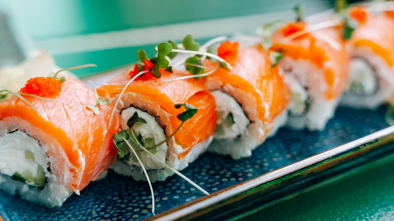 uramaki sushi rolls with salmon, cream cheese, cucumber, microgreens, and roe, beautifully presented on a blue plate