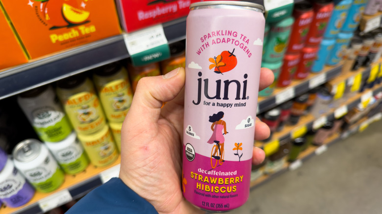 Hand holding Juni adaptogenic decaffeinated strawberry hibiscus tea in grocery store