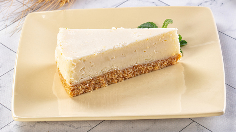 Slice of New York classic cheesecake on square cream plate with mint