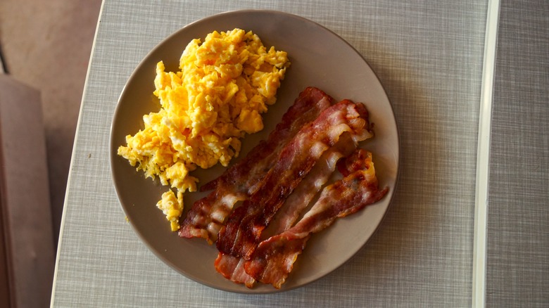 scrambled eggs with bacon on a plate on a grey table