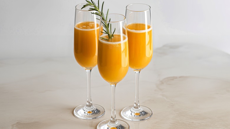 three champagne flutes filled with orange mimosa cocktail, the front glass has a sprig of rosemary