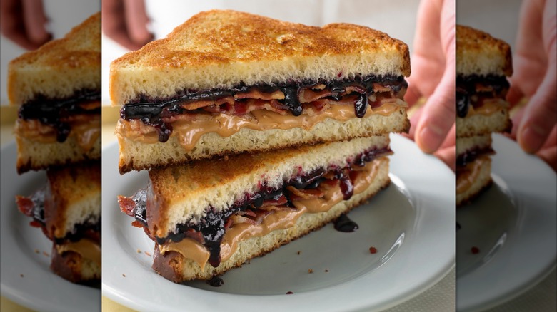 Stacked peanut butter bacon sandwich on white plate with hands in background, mirrored image