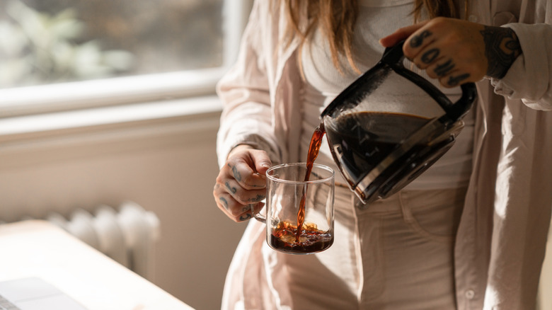 A woman pours coffee into a clear mug