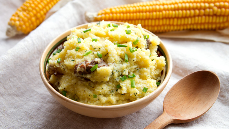 bowl of Cornmeal mush with meat and onion, next to corn and wooden spoon