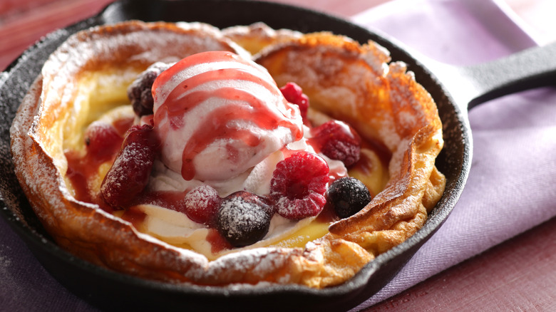 a Dutch baby pancake, served in a cast-iron skillet with fresh berries, vanilla ice cream, and a drizzle of sauce