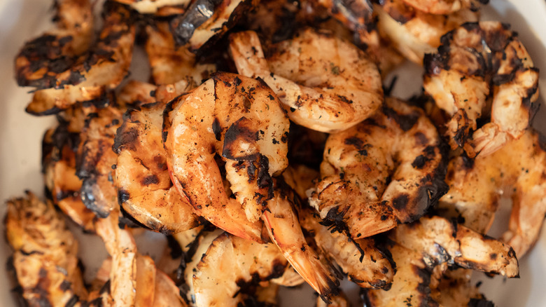 a plate filled with lightly charred shrimp, with shells off but tails left on