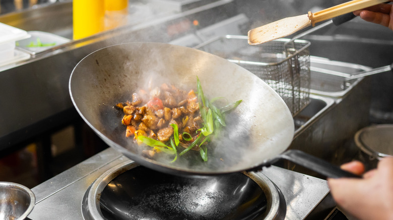 chef in an Asian restaurant tossing meat and vegetables in a wok at high temperature, over a specialized commercial wok burner