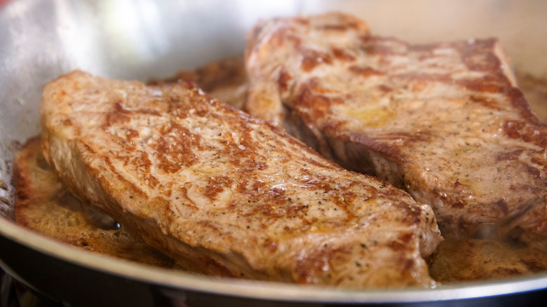 a pair of steaks browning in a hot skillet