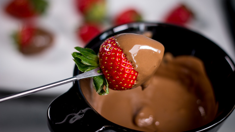 Close-up of strawberry on metal skewer over melted chocolate pot.