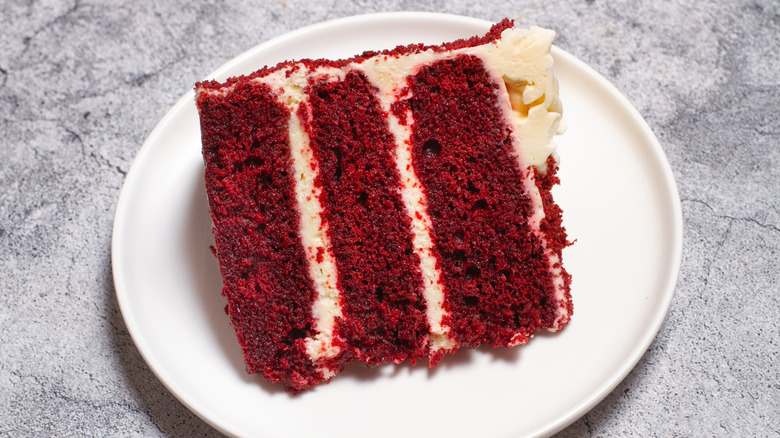 A piece of red velvet cake on a white plate on gray table.