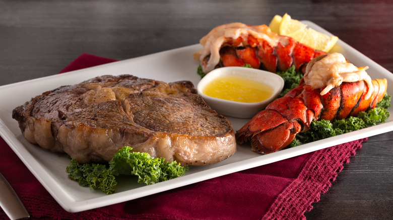 White plate of steak and lobster tail, on red napkin.