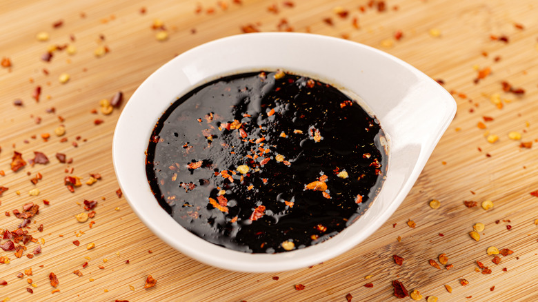 Bowl of teriyaki sauce with chili flakes on bamboo board.