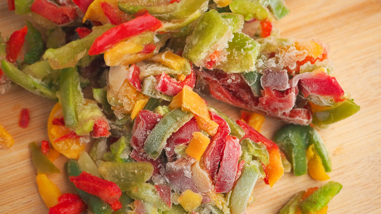 frozen mix of colorful red, green, and yellow peppers on a pale-colored wooden cutting board