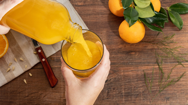 Person pouring orange juice from bottle into glass