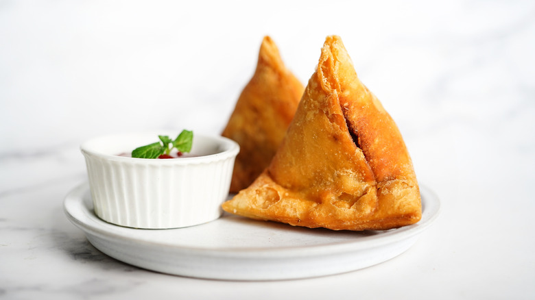 Two samosas on plate with bowl of chutney
