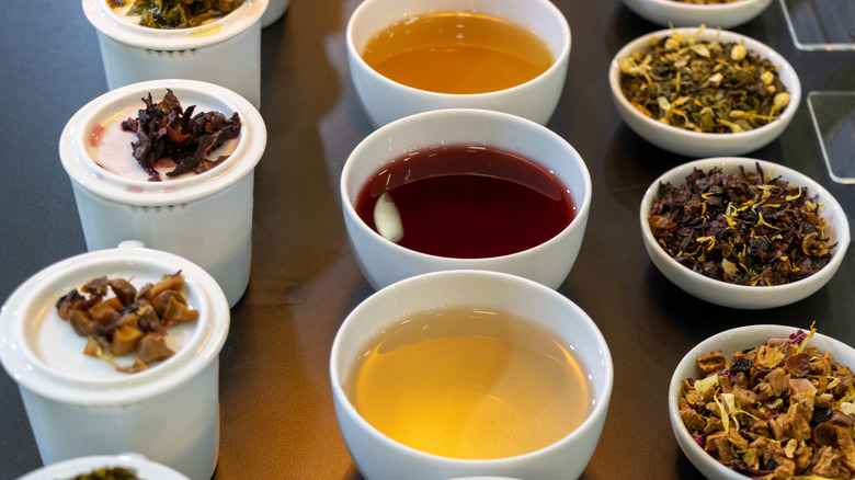 Assortment of herbal teas in cups with dry blends adjacent