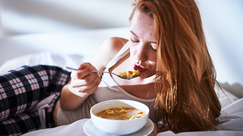 Woman in bed eating chicken noodle soup
