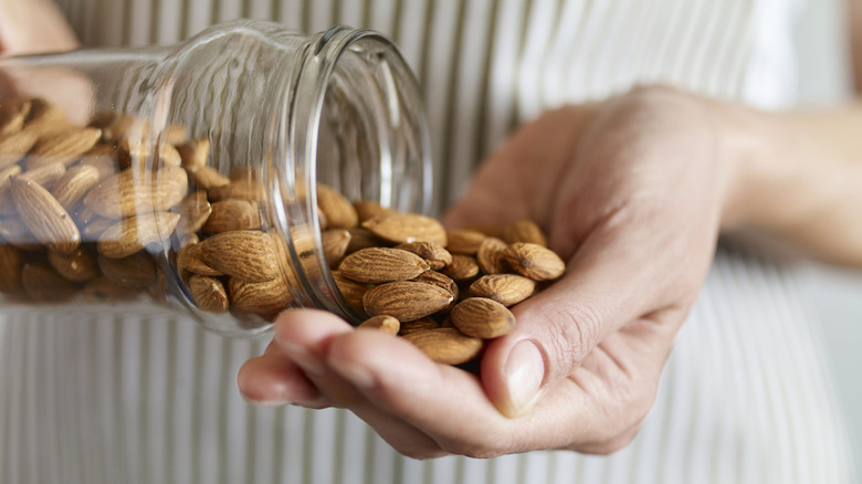 A person pours a handful of almonds from a glass jar