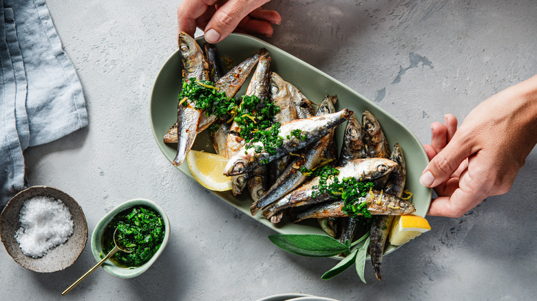 A plate of grilled sardines with herbs and lemon wedges