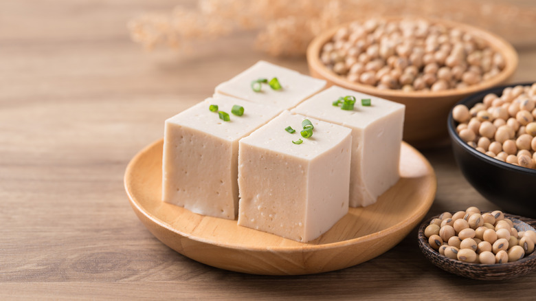 Fresh tofu cubes next to bowls of dry soybeans