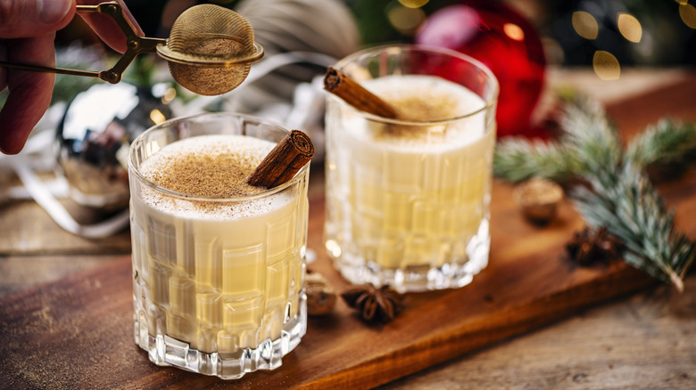 two crystal glasses of eggnog with a cinnamon stick in each