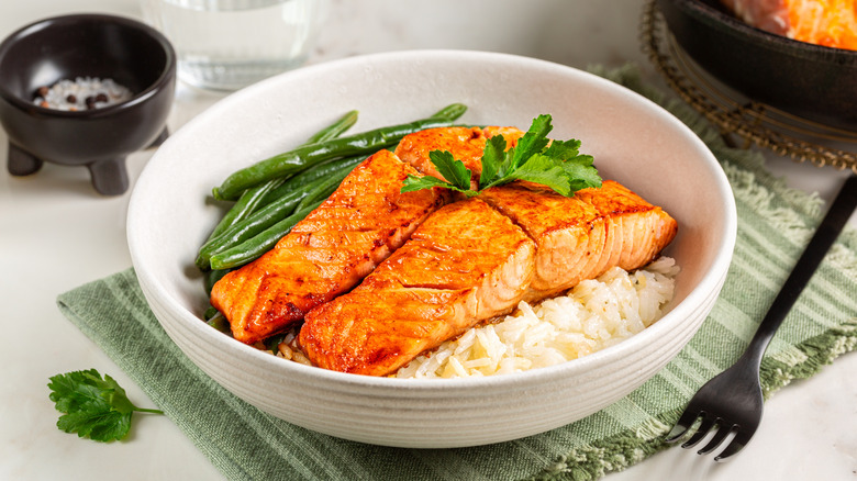 two filets of glazed salmon in a white bowl with green beans and rice