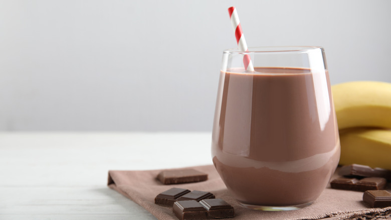 a glass of chocolate milk with a red and white straw and chocolate pieces scattered around