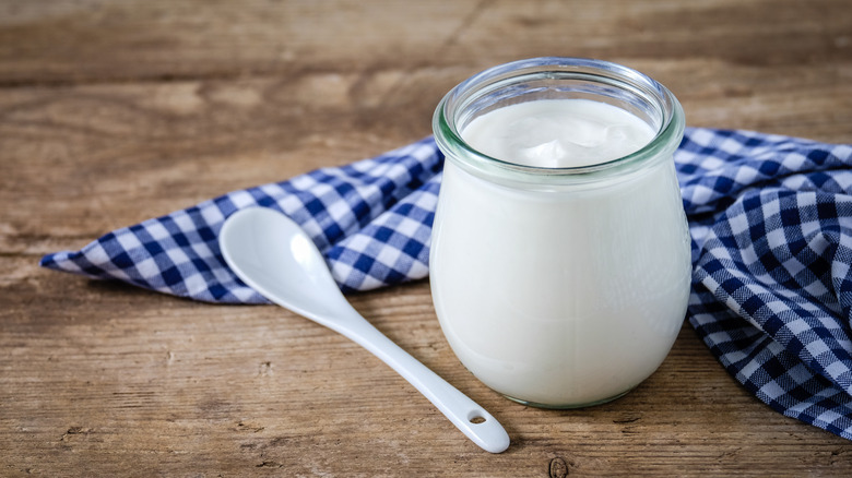 a glass jar of yogurt with a blue gingham cloth and spoon