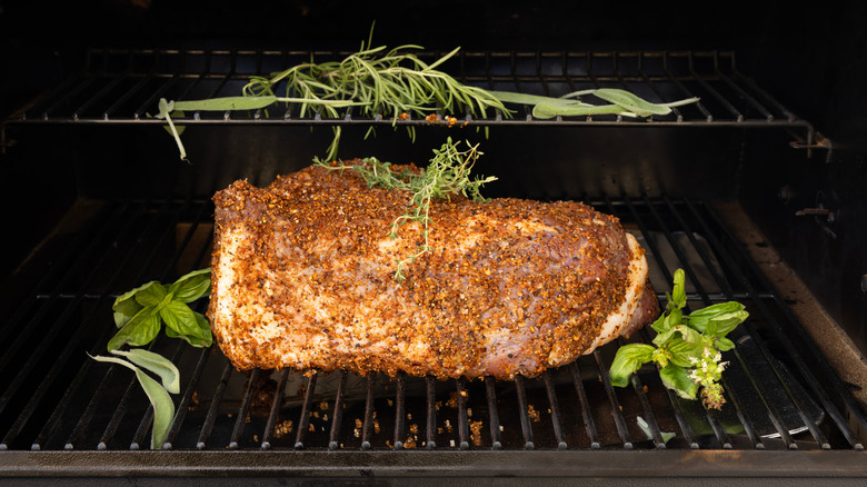 A seasoned chuck roast on a grill surrounded by fresh herbs