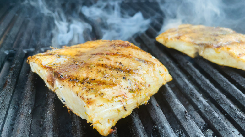 Two pieces of fish being grilled over indirect heat