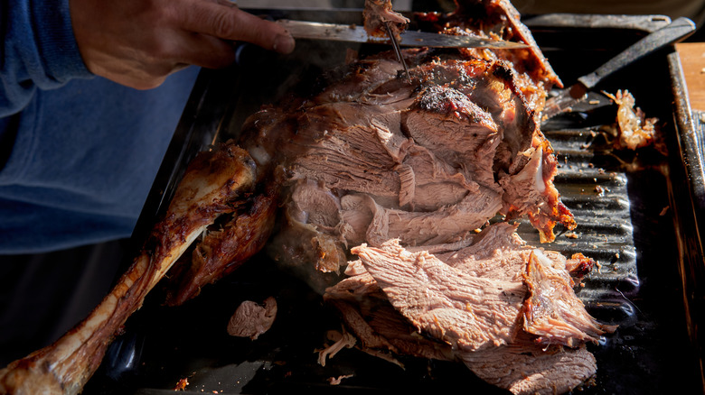 Leg of lamb being sliced directly on an Argentinian grill