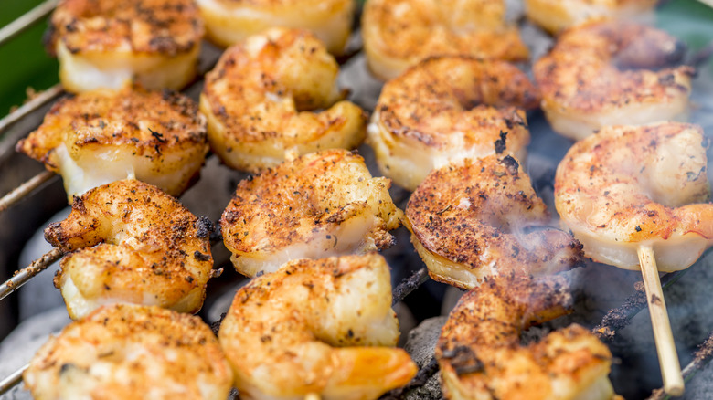 A closeup of shrimp on wooden skewers being grilled