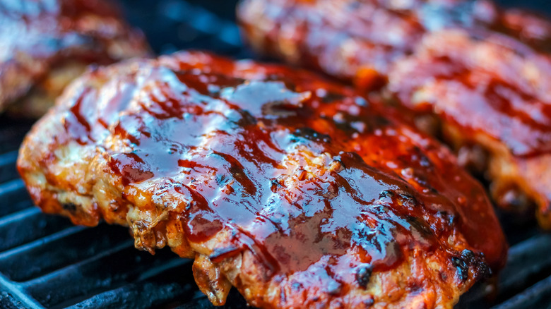 A closeup of highly sauced small racks of rib on the grill