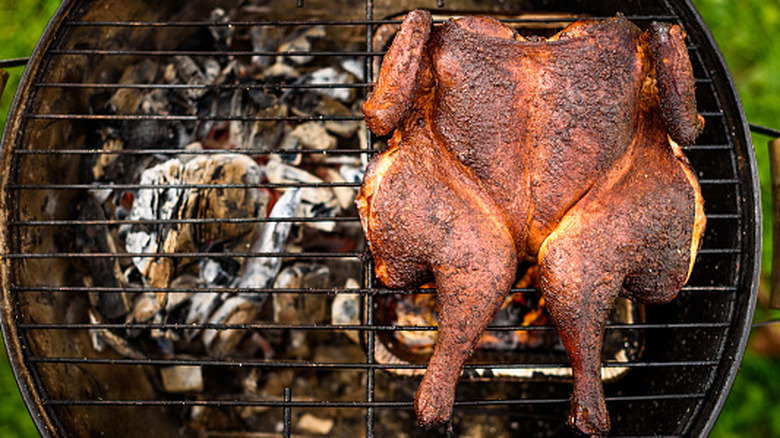 A whole chicken that has been spatchcocked and placed on a grill, with a drip pan below it
