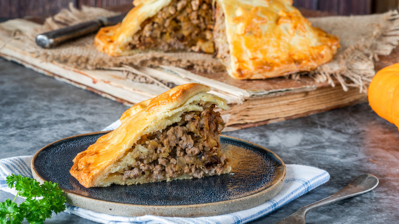 A slice of apple pork pie on a plate with a full apple pork pie in the background