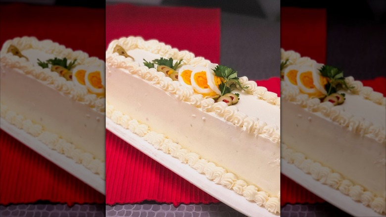 Frosted sandwich loaf topped with boiled eggs, olives, and herbs