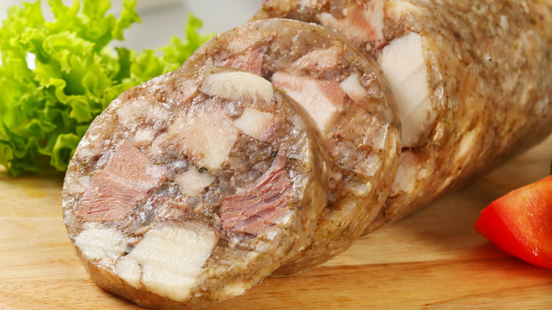 Sliced head cheese sausages with lettuce and tomato in the background