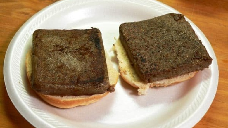 Two squares of fried liver mush on top of bread in a styrofoam plate