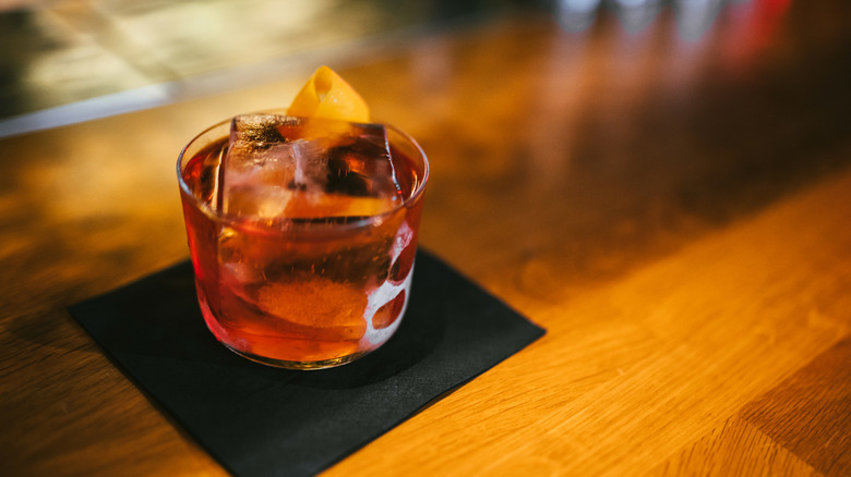 Gin and vermouth in crystal glass with orange slice on a black cocktail napkin on a bar.