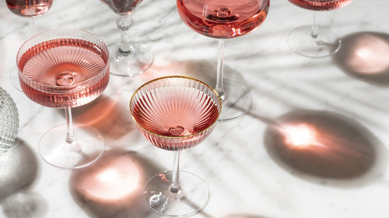 Pink gin cocktail in coup glass with sunny summer light on white marble table and shadow.
