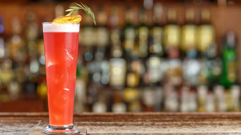 Cocktail singapore sling on the bar with the liquor shelf blurry in the background.