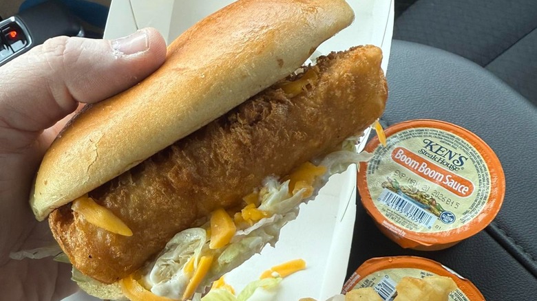 Hand holding Culver's fish sandwich in a car with Ken's boom boom sauce