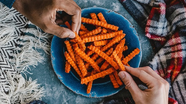 Hands reaching for Culver's sweet potato fries on a plate on top of blankets
