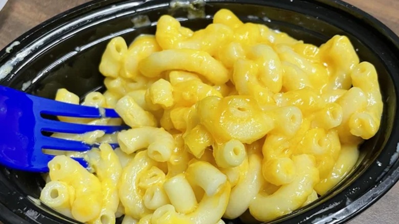 Unmixed mac and cheese in black plastic dish with blue fork