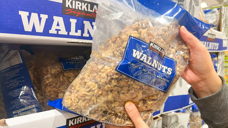 Hands holding a bag of Kirkland walnuts in front of a Costco walnut display