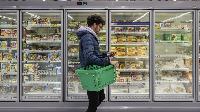 Person looking at phone while shopping in freezer aisle of grocery store