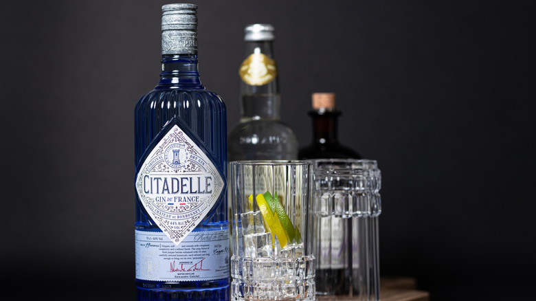 French Citadelle gin, in elegant blue bottle with crystal highball glass on wooden serving board.
