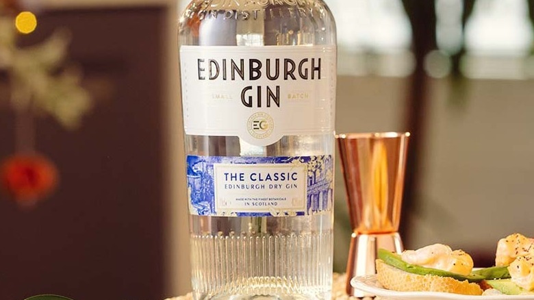 Close up of bottle of Edinburgh Gin next to copper jigger and plate of food.