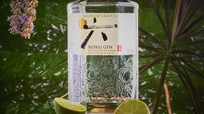 Close up of Roku gin with halved limes and plants in the background.